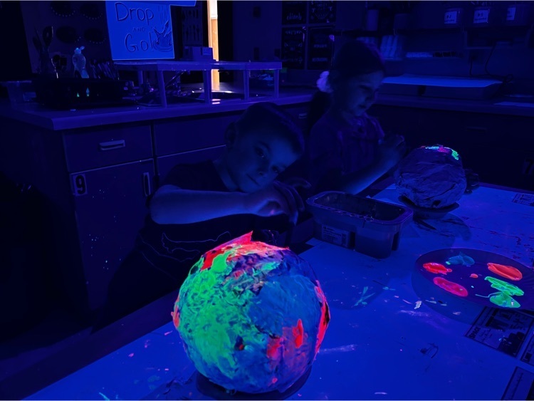 students painting their paper mache planets with neon paint in black lit room